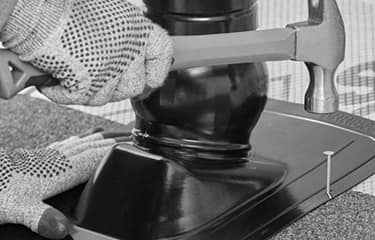 Shaded image of a GAF roofer’s gloved hands using a hammer and nail to install Master Flow Pivot Pipe Boot Flashing to a residential roof