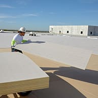 roofer carrying cover board across roof deck