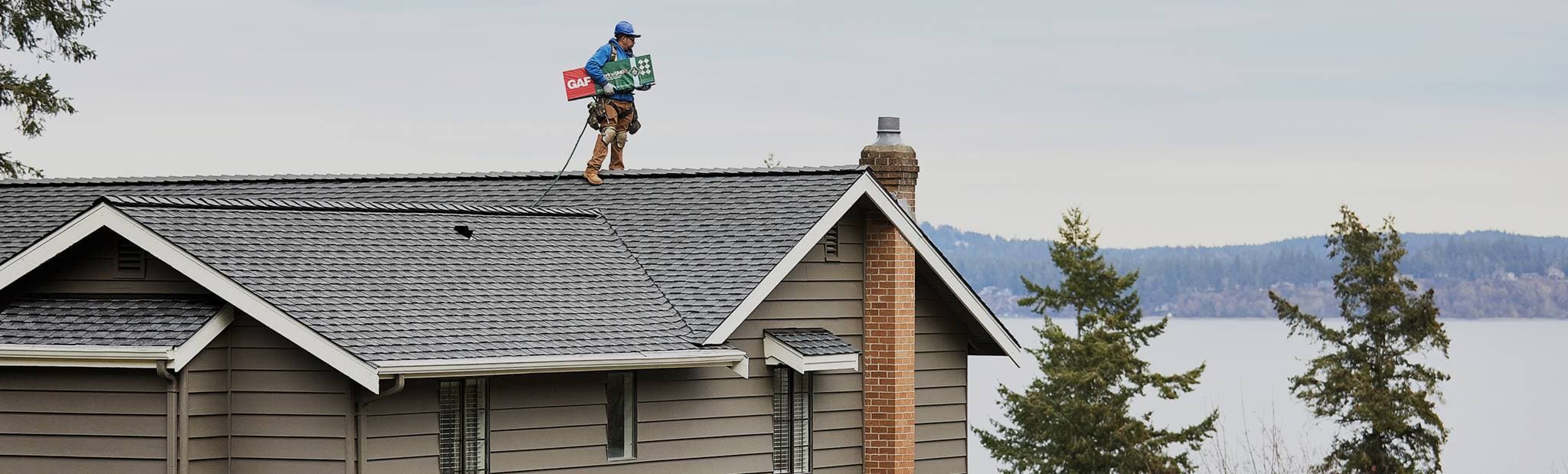 GAF contractor on a new roof with gray Timberline HDZ shingles overlooking a lake and mountains