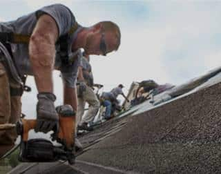 Roofer using a nail gun to secure new GAF shingles on a pitched roof