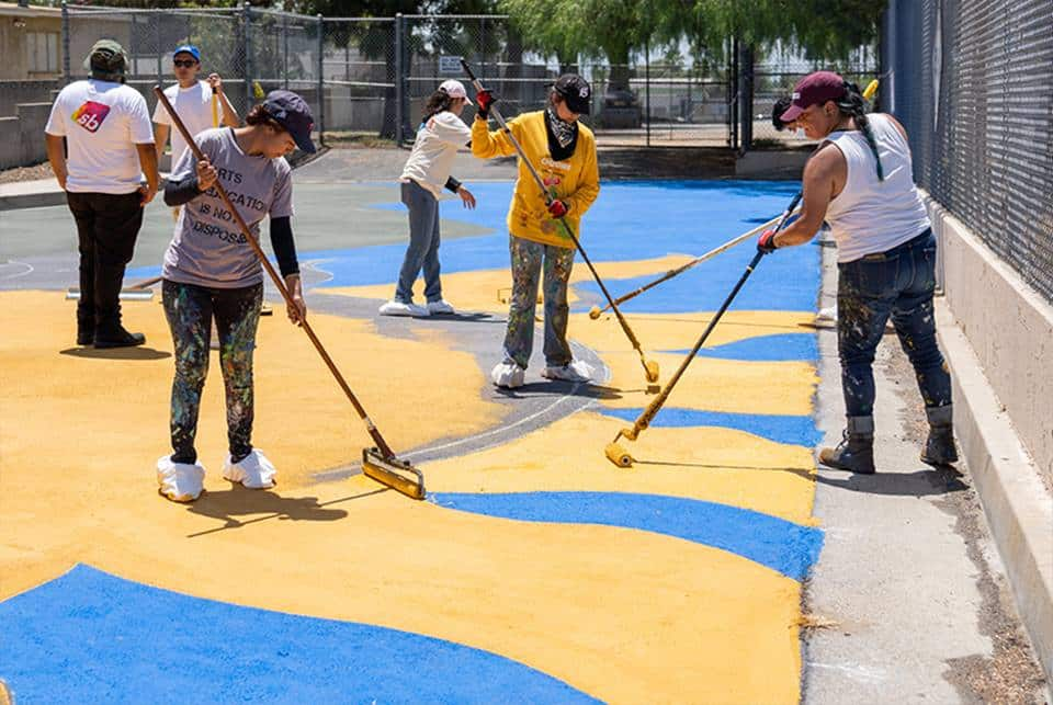 Community members helping to paint StreetBond onto asphalt as part of GAF’s Cool Community Project.