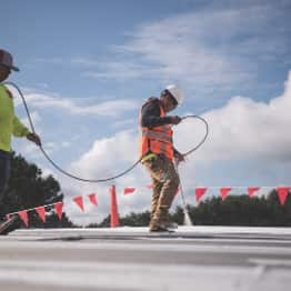 roofer spraying roof coating over a low-slope roof deck