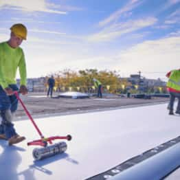 roofer spreading out tpo membrane over roof deck